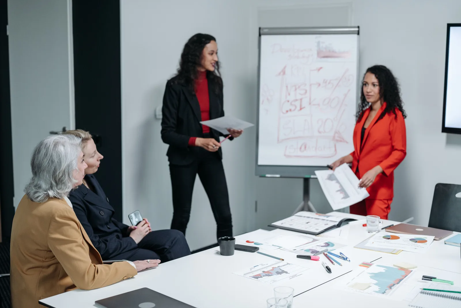 A diverse group of business professionals reviews charts and discusses career and business plans in an office.