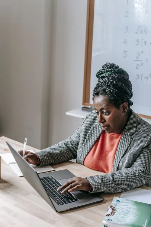 A postgraduate student works on a laptop in a bright study space.
