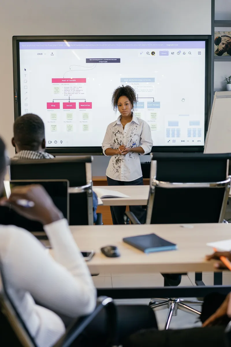 A professional woman leads a meeting with a diverse team, using a digital display.