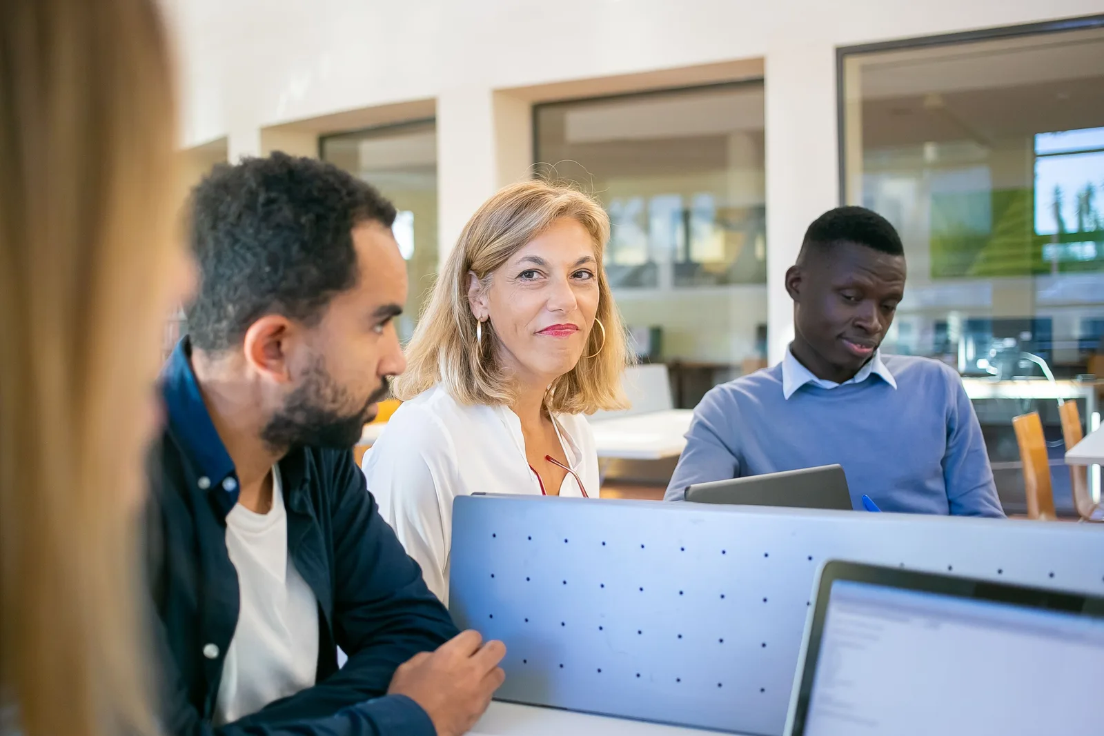 Adult learners work at computers in a classroom while another learner sits beside them.